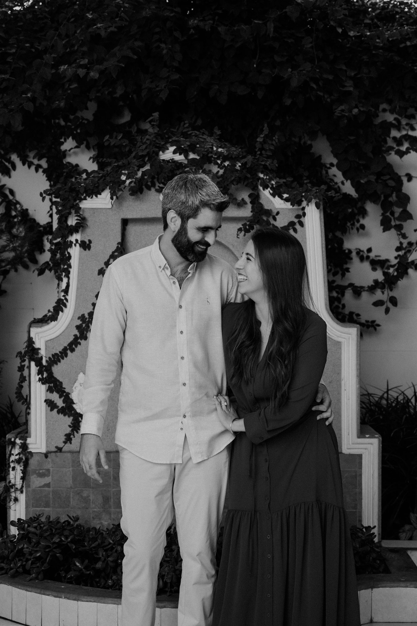 María Paula y Matías en blanco y negro, sonriéndose frente a una pared cubierta de hiedra